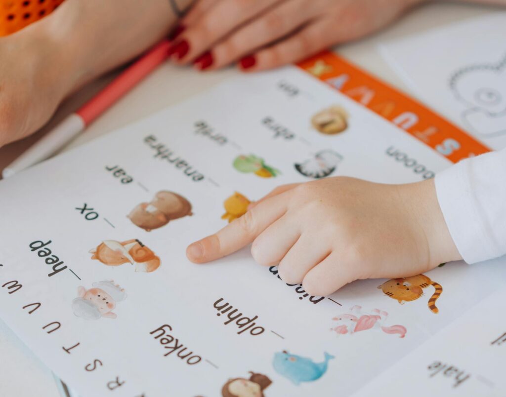 A child points to animals in a colorful alphabet book, learning letters.