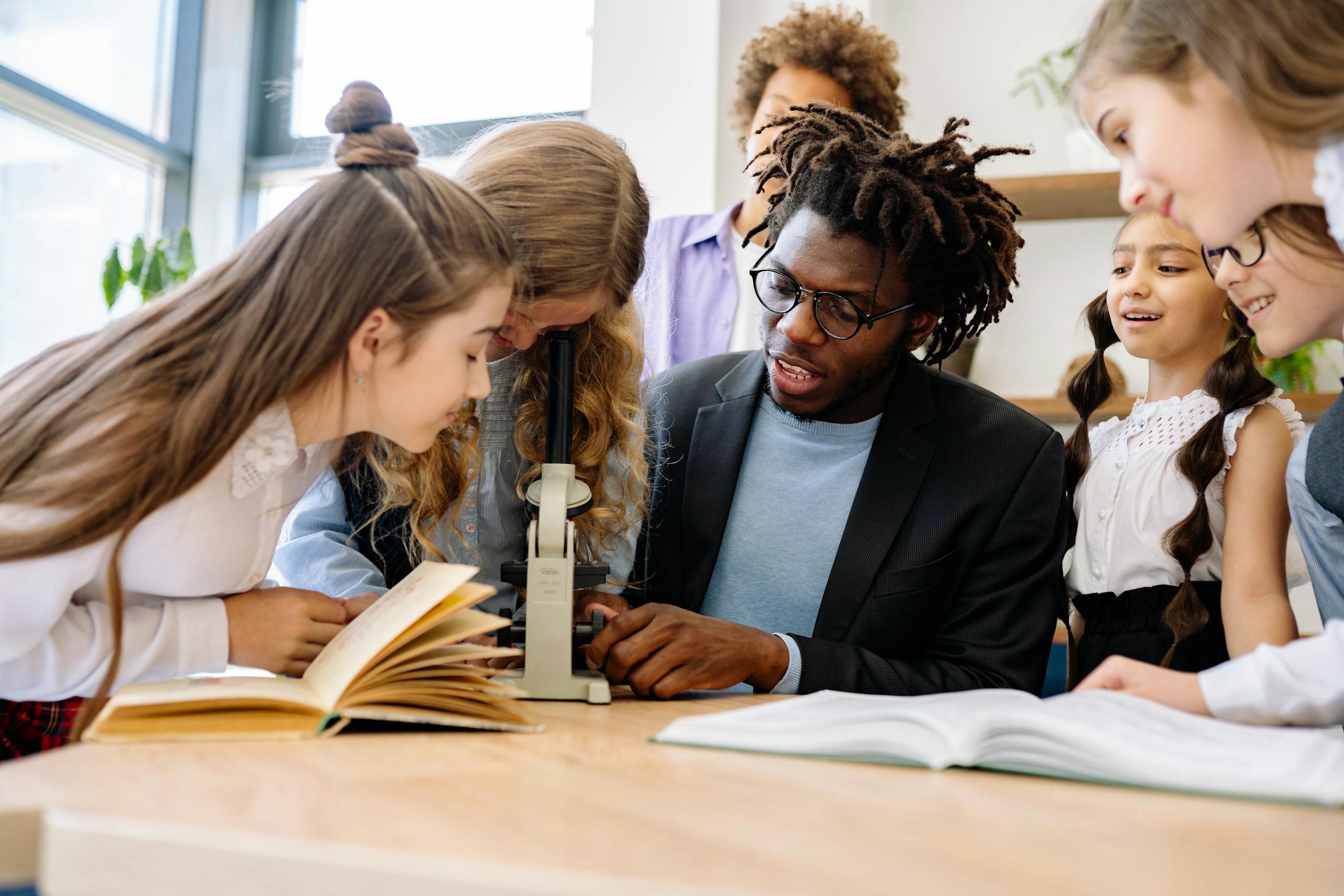 Photo by Yan Krukau Students and teacher engage in science lesson using a microscope, fostering curiosity and learning.