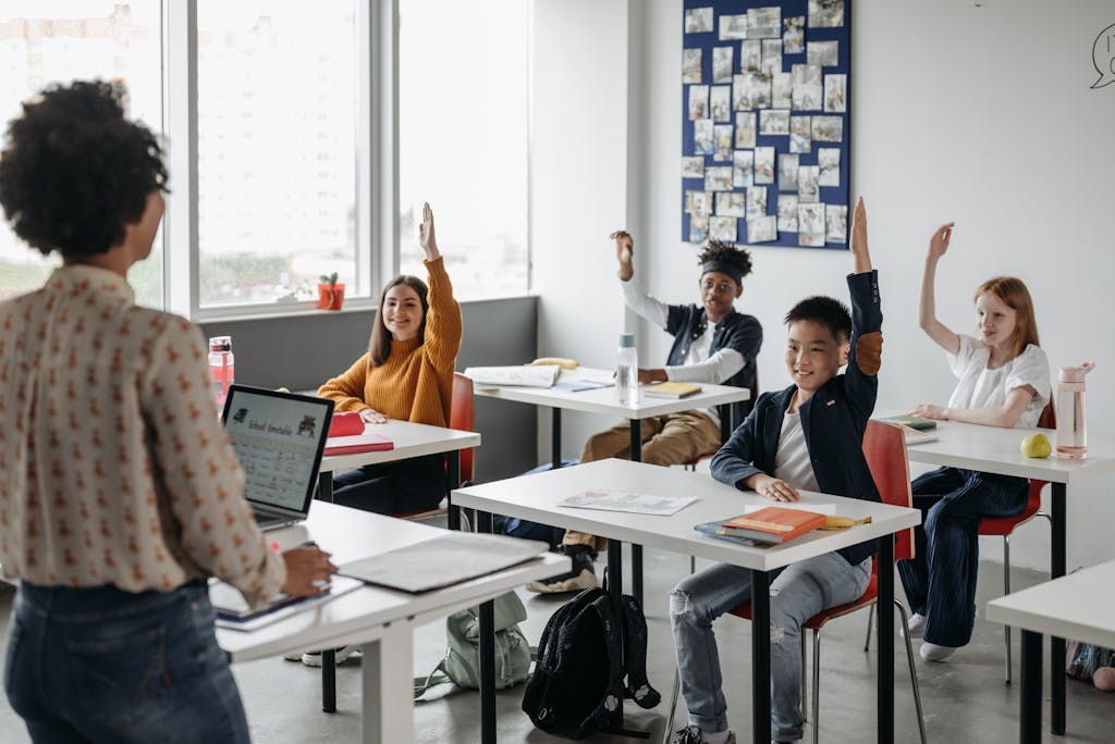Students in a diverse classroom eagerly raising hands during a lesson. Bright, educational atmosphere.
