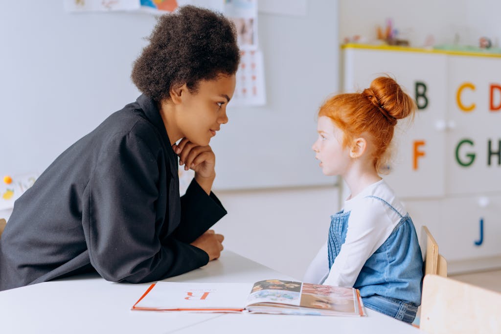 An adult teacher and a child student engage in a learning session at a classroom table.
