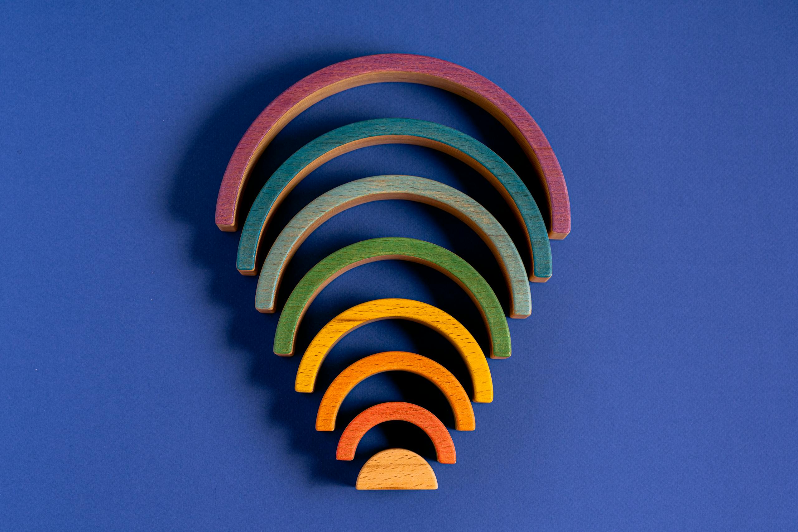 Vibrant rainbow-colored wooden arches arranged in a pattern on a blue background.