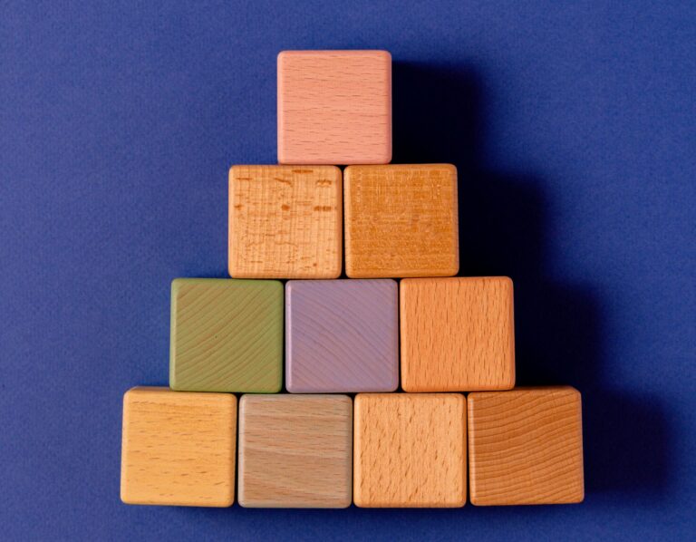 Colorful wooden blocks stacked in pyramid shape on a blue backdrop.